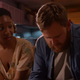 Two people sit on a couch in a kitchen in As Dusk Falls.